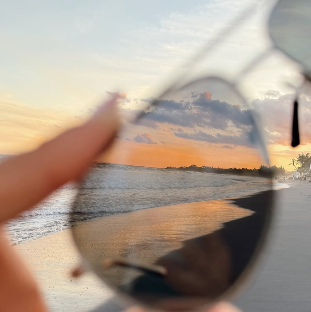 Sunglasses on a beach looking at the sunset through Revo lenses